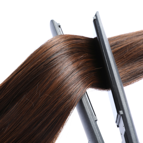 Hair straightener being used on a section of brown hair against a white background