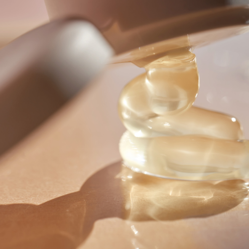 Close-up of a hand holding a bottle with a pump dispenser, filled with a beige liquid which contains with Cacay oil