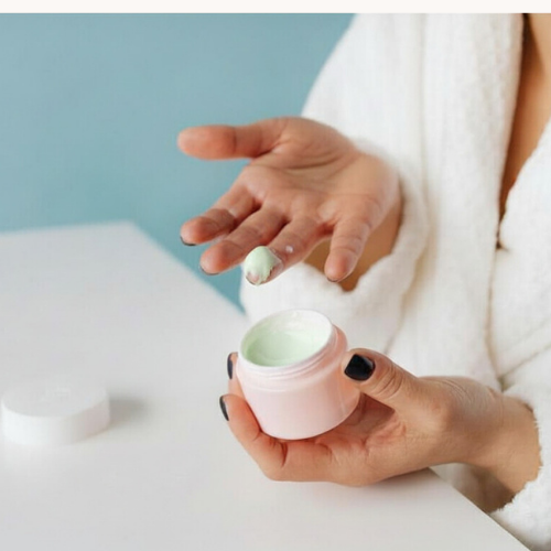 Person holding a small pink container with a cosmetic product with Açai oil, against a light blue background.