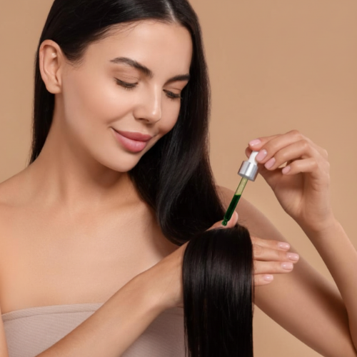 Woman holding a dropper with green liquid near her hair against a beige background