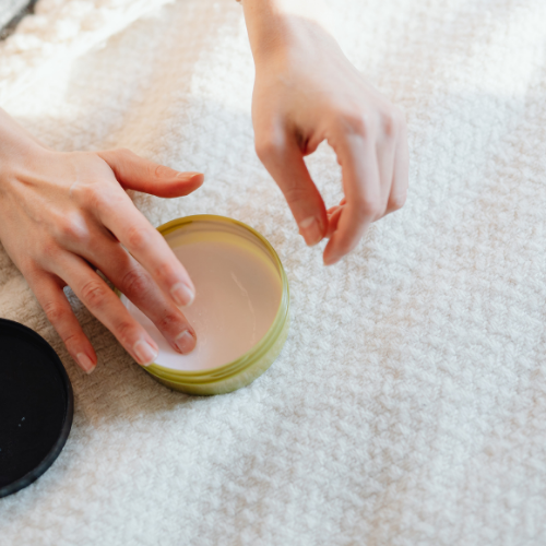 Person holding a small container with murumuru butter on a textured white surface