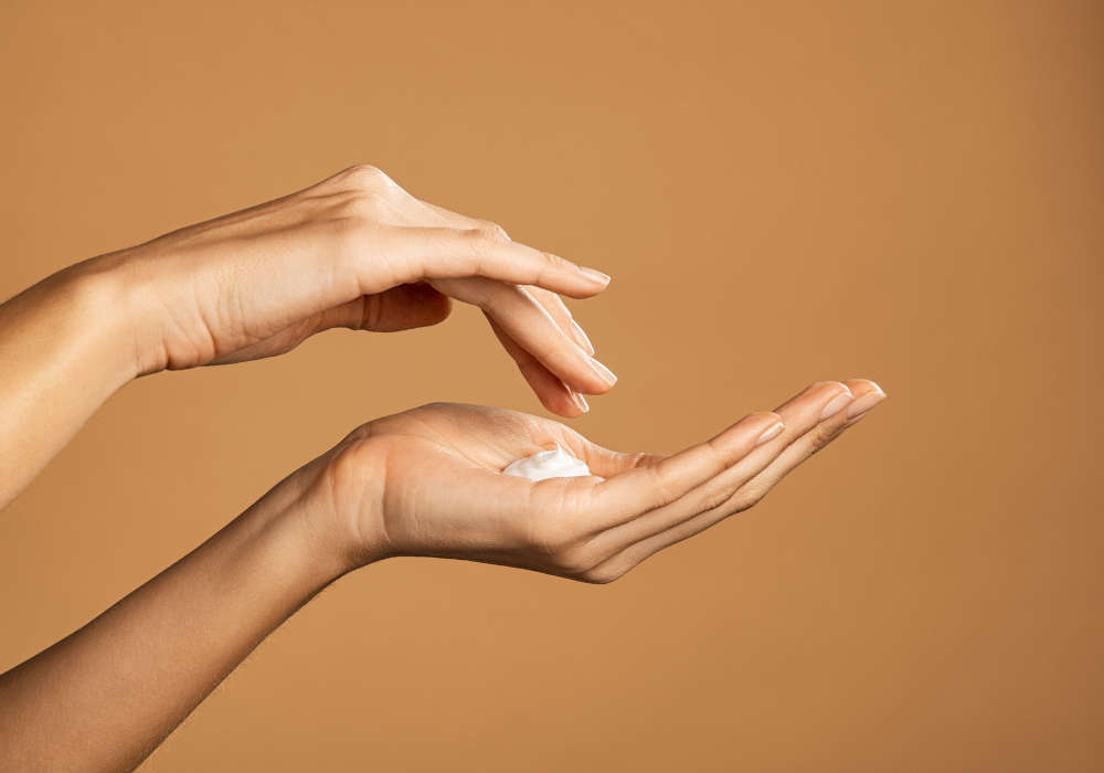 Two hands holding a small amount of cream against a brown background
